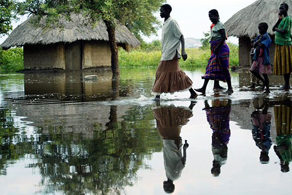 Ugandan women and children walk past submerged homes in an area flooded by heavy rains in Soroti, Uganda, Sept. 18 2007.